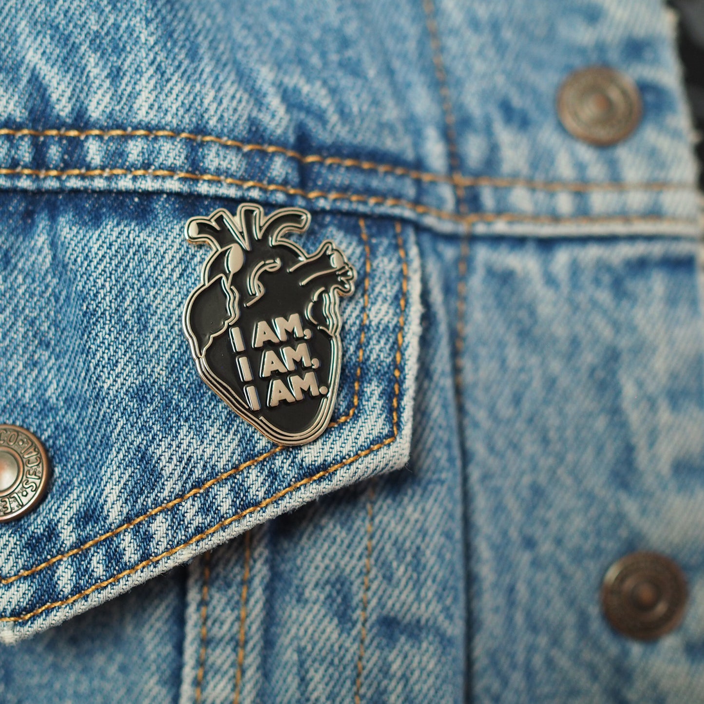 Close up on denim jacket of the Black Anatomical Heart enamel pin featuring a quote by Sylvia Plath Bell Jar - Feminist Poet Writer